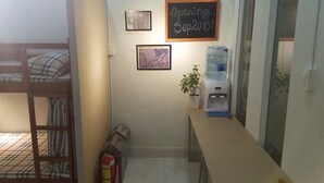 A small room with a bunk bed, a desk with a water dispenser, a fire extinguisher, and a chalkboard sign indicating an opening date. - Natural House Hostel (Ho Chi Minh City)