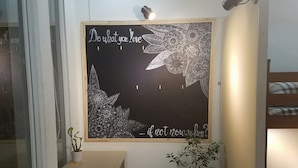 A room with a chalkboard wall featuring a motivational quote, a wooden bench, a potted plant, and a bunk bed. - Natural House Hostel (Ho Chi Minh City)