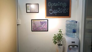A wall with a framed map, a framed map with text, a chalkboard sign, a water dispenser, and a potted plant. - Natural House Hostel (Ho Chi Minh City)