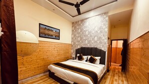 A bedroom with a wooden headboard, a bed with white bedding, a ceiling fan, and a patterned wall. - New Basera Hotel (Ukhimath)