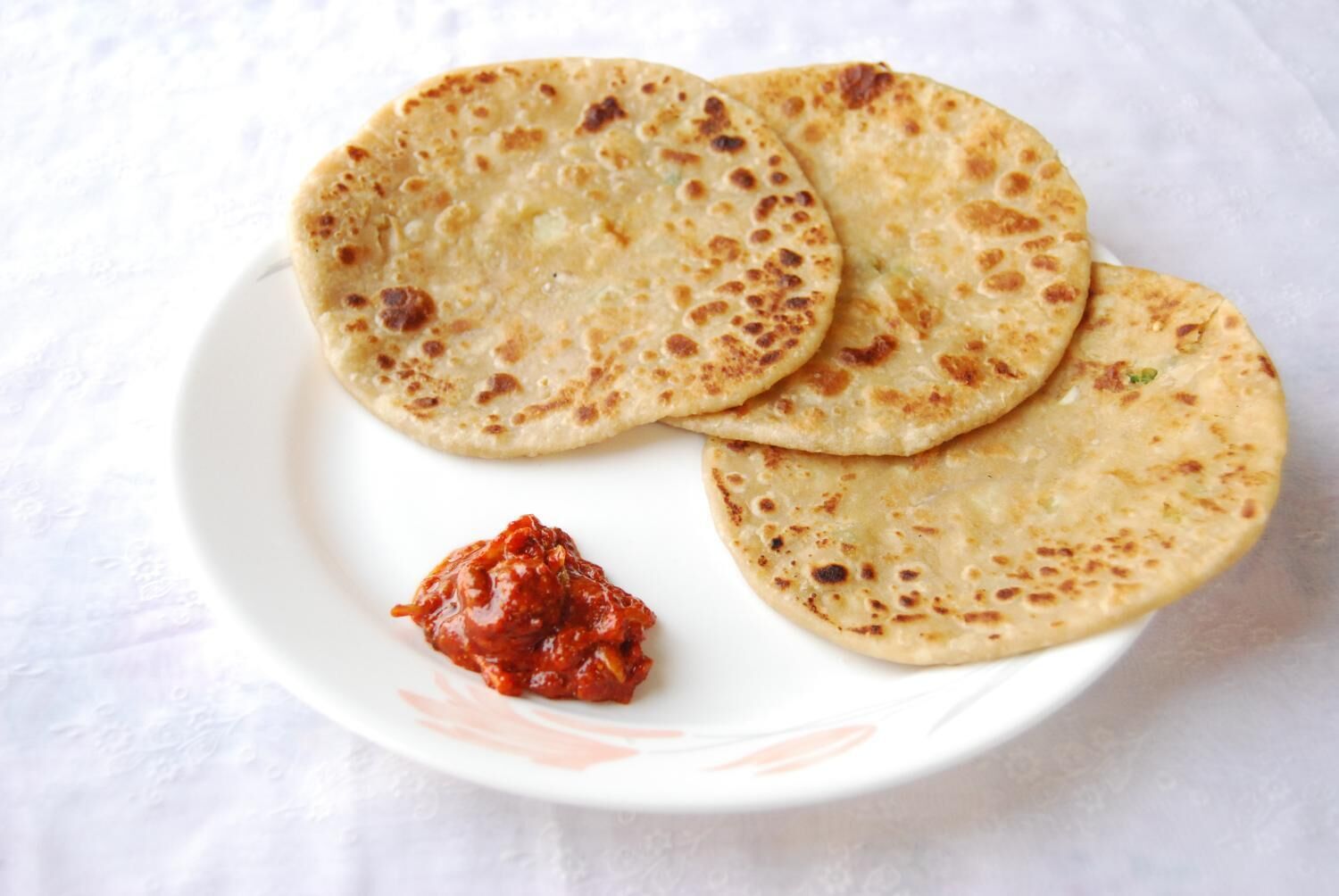 Un plato con tres panes planos y una porción pequeña de salsa roja.