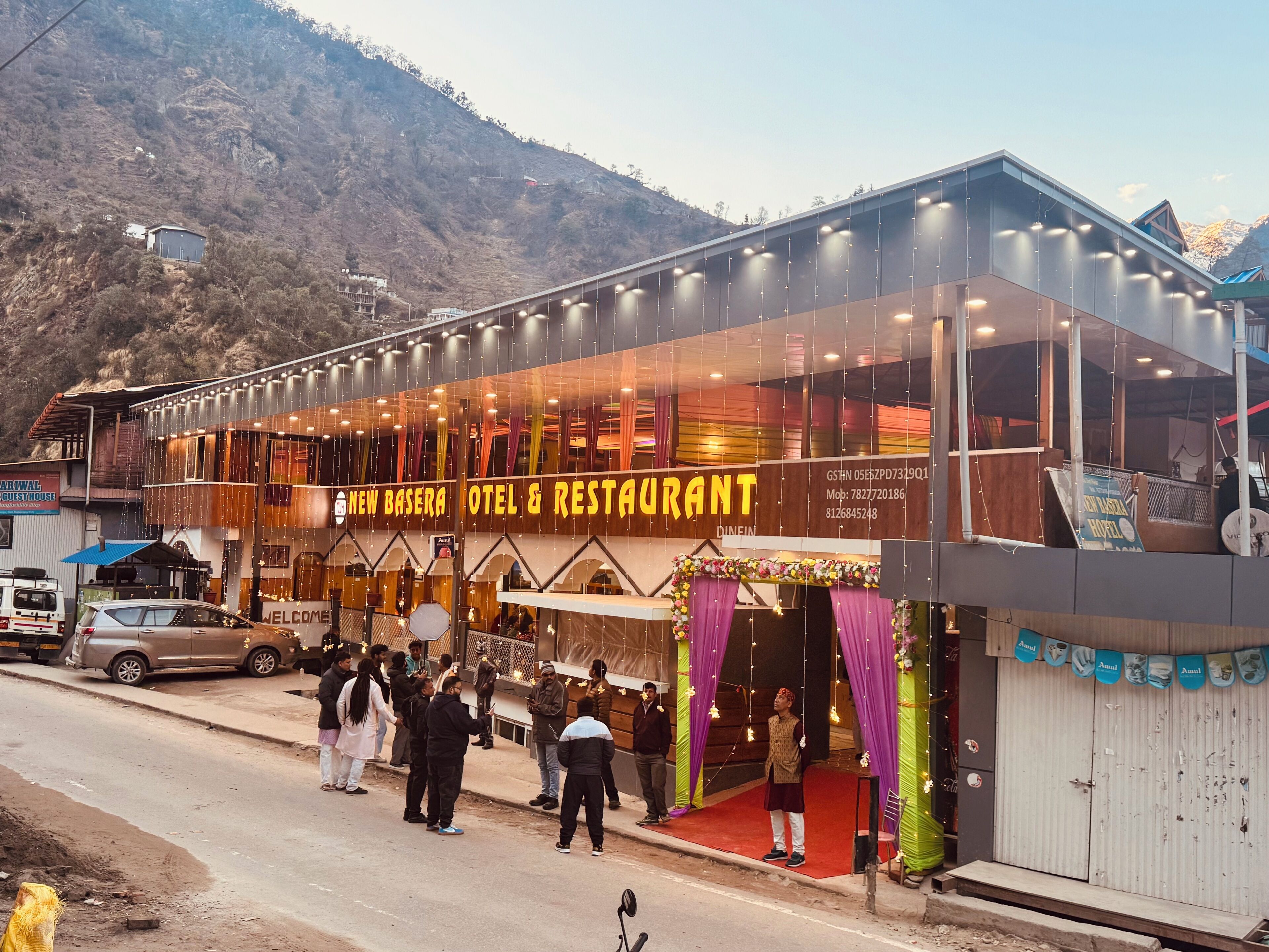 A hotel with a modern glass facade, a red carpet entrance, and a mountainous backdrop.