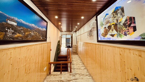 A hallway with wooden paneling, a staircase, and two large framed pictures on the walls. - New Basera Hotel (Ukhimath)