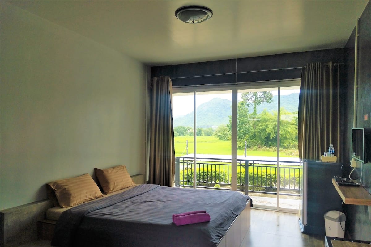 A bedroom with a large bed, a desk, and a view of a green landscape through the window.