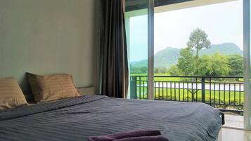Un dormitorio con una cama grande y vistas a un paisaje verde a través de un balcón.