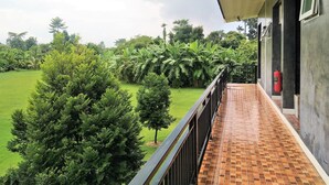 Een balkon met betegelde vloer, omringd door weelderige begroeiing en uitzicht op een grasveld.