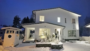 Una casa de dos pisos con una entrada bien iluminada, el número '10' visible en la fachada y un paisaje cubierto de nieve.