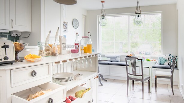 Una cocina luminosa con armarios blancos, un comedor con mesa y sillas, y un amplio ventanal que proporciona luz natural.