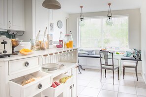 A bright kitchen with white cabinets, a dining area with a table and chairs, and a large window providing natural light. - Villa Jokivarsi B&B (Vantaa)
