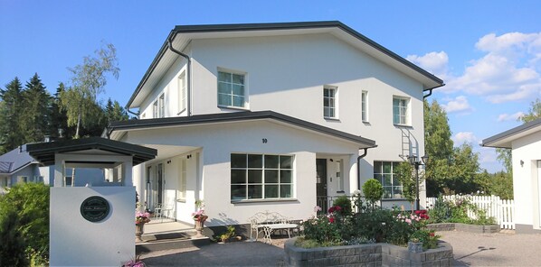 A two-story building with a white exterior, a covered porch, and a small garden with flowers. - Villa Jokivarsi B&B (Vantaa)