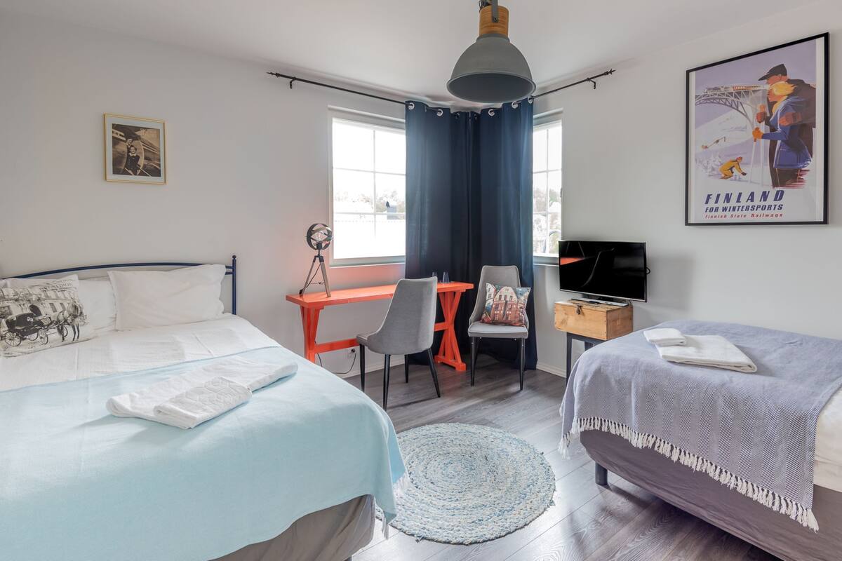 Une chambre d’hôtel avec deux lits, un bureau, une chaise, une télévision et une affiche au mur.