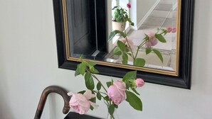 Un espejo con marco negro y un florero con flores rosadas sobre un tocador oscuro.