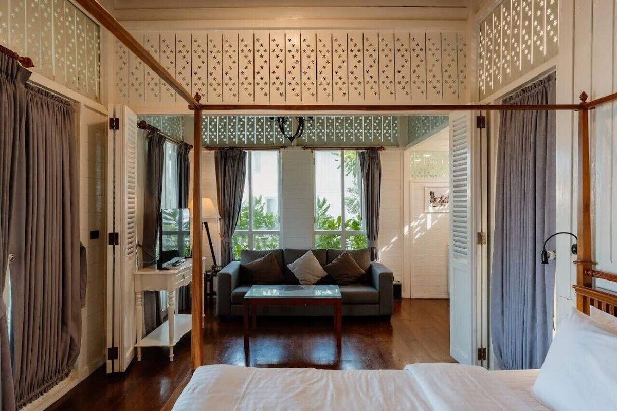 A room with a bed, a sofa, and a TV. There is a window with curtains, a ceiling with star patterns, and a wooden floor.