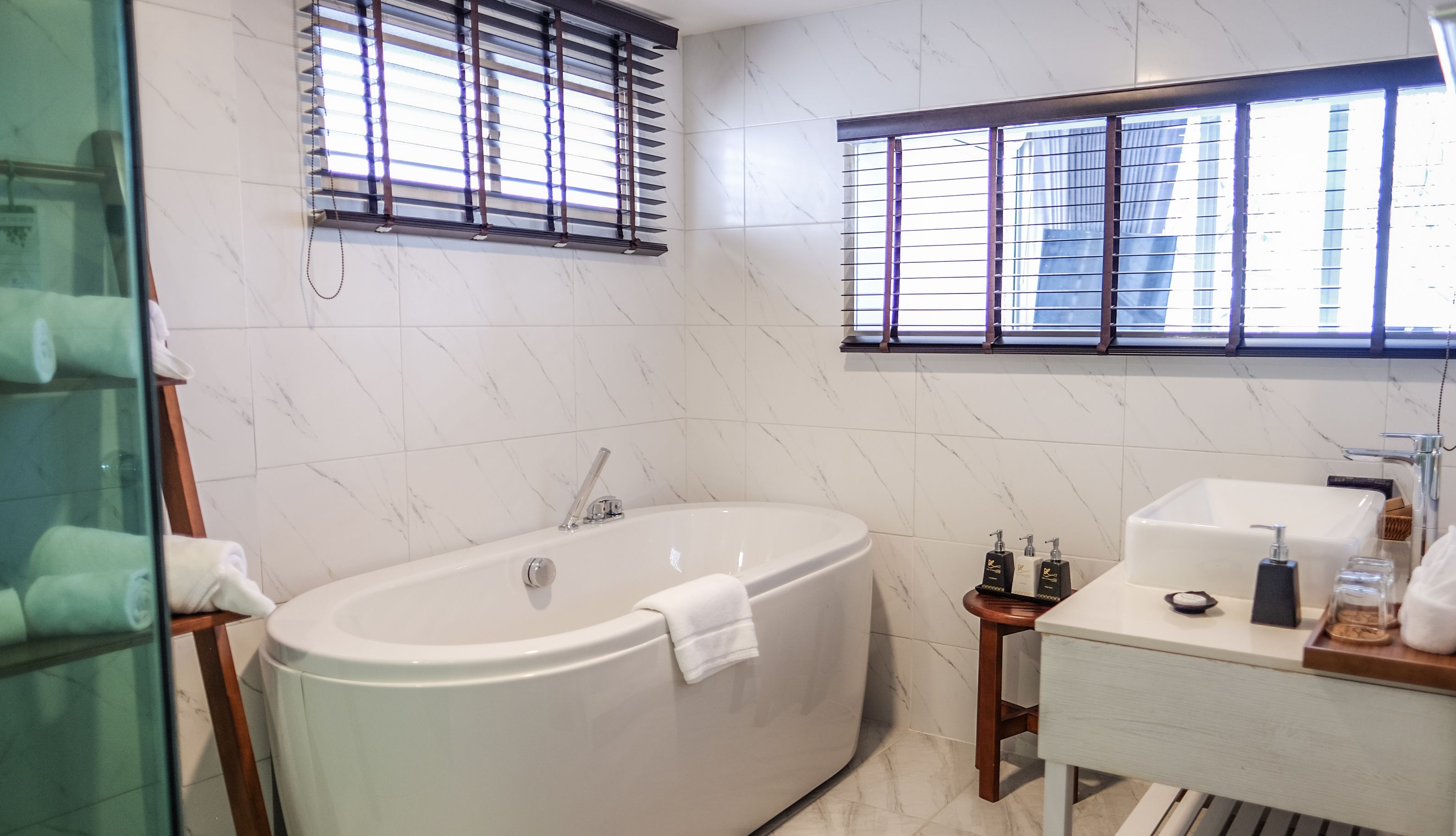Un baño moderno con una bañera independiente, un lavabo y una ventana con persianas.
