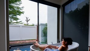 A person relaxing in a bathtub with a view of a swimming pool and a garden outside. - De Chaochom Hua Hin (Hua Hin)