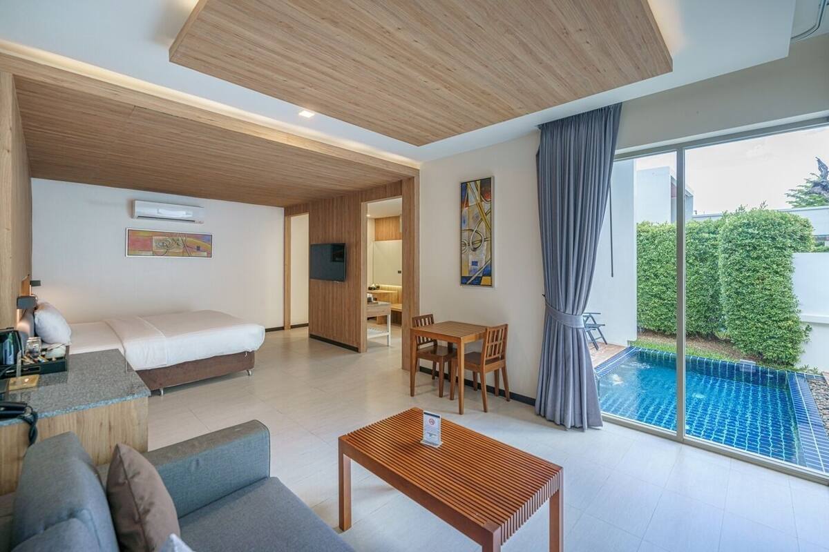 A modern hotel room with a bed, a sofa, a dining table, and a view of a swimming pool.