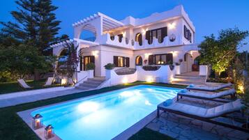 A modern villa with a swimming pool, outdoor seating, and a well-lit entrance.
