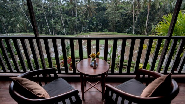 A balcony with two wooden chairs and a small table with a vase of flowers. - Niniku villa (Tegallalang)