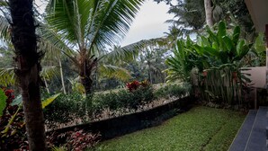A lush garden with palm trees, a stone wall, and a tiled pathway. - Niniku villa (Tegallalang)