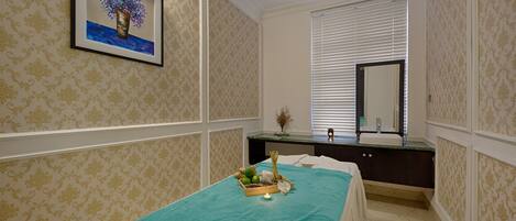 A spa room with a bed, a vanity, a mirror, and a framed artwork on the wall.