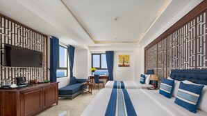 A hotel room with a large bed, a desk, a sofa, a TV, and a view of the sea. - Eden Hotel (Da Nang)