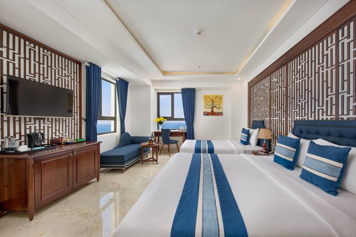 Une chambre d’hôtel avec un grand lit, un bureau, un canapé, une télévision et une vue sur la mer.