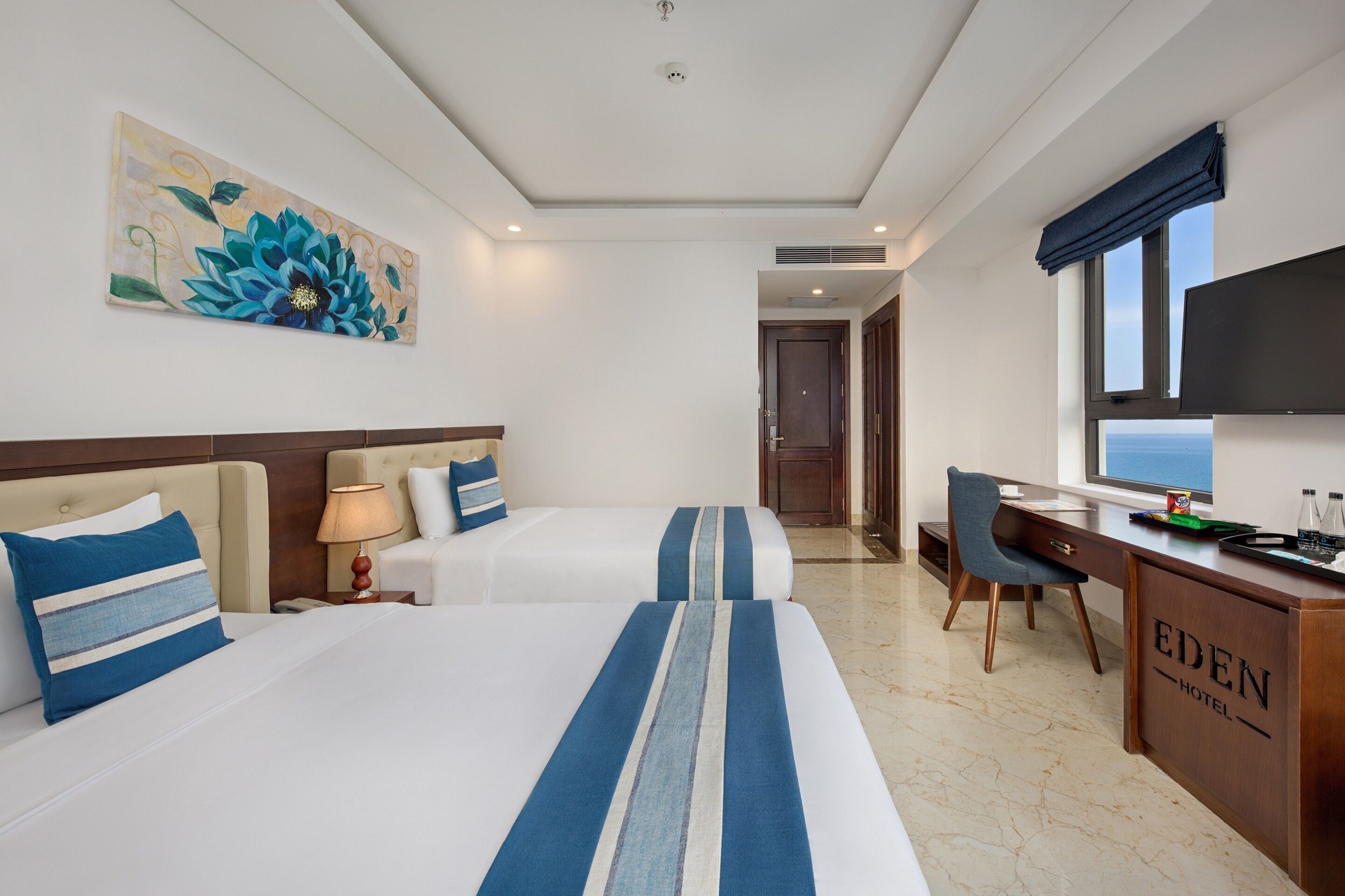 A hotel room with two beds, a desk, a chair, and a large window.
