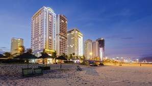 A beachfront hotel with multiple high-rise buildings, palm trees, and beach chairs. - Eden Hotel (Da Nang)