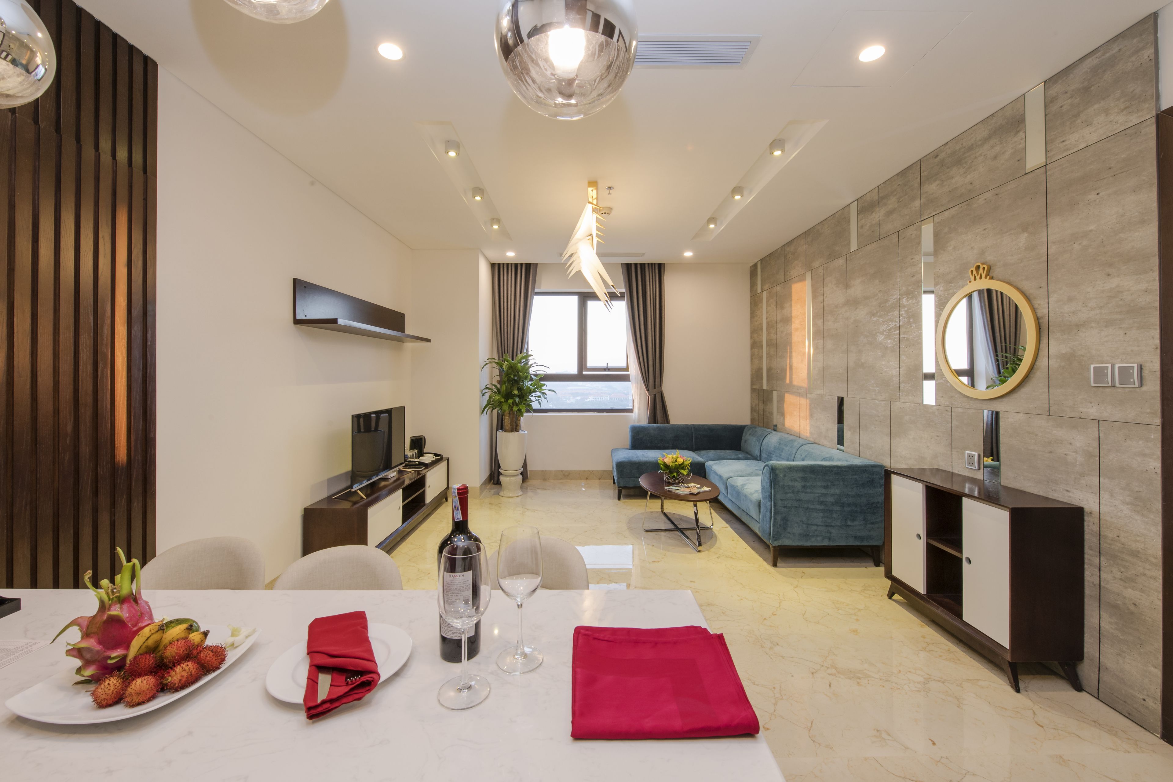 A modern living room with a sofa, a dining table set with a bottle of wine, fruit, and glasses.