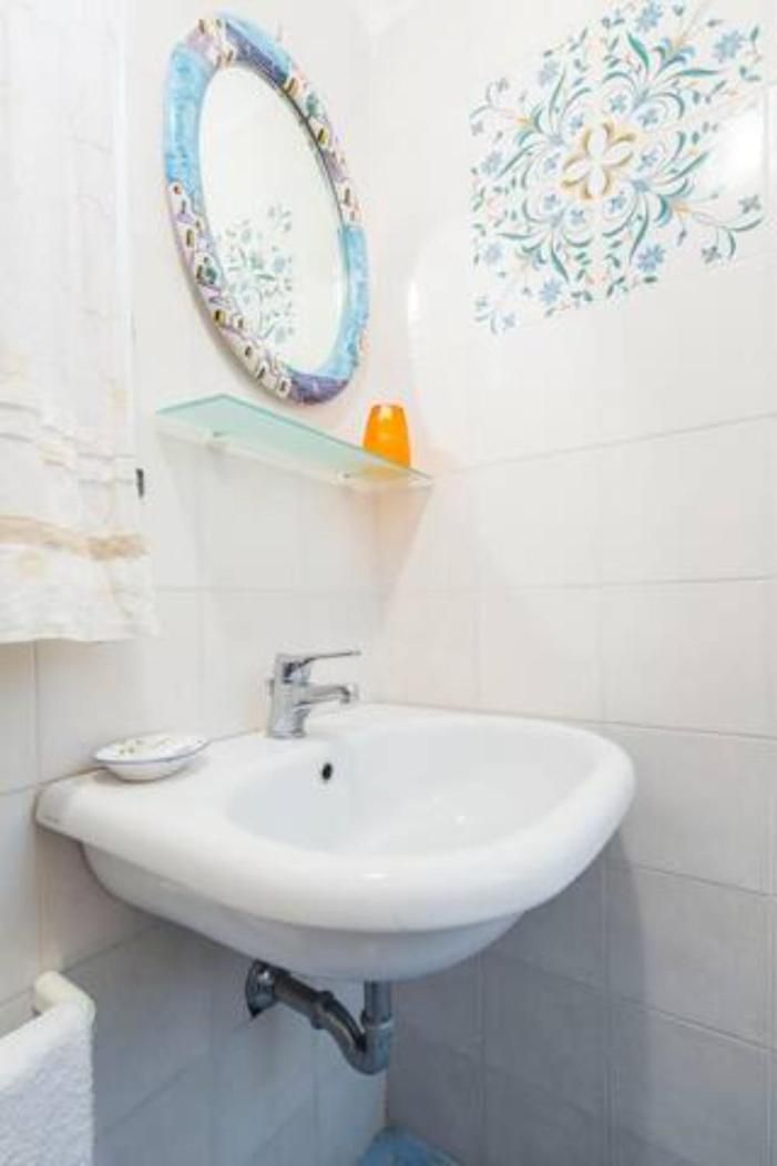 Een badkamer met een witte wastafel, een spiegel met decoratieve lijst en een wandtegel met een bloemendesign.