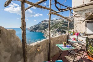 A balcony with a view of the sea, a table with chairs, and potted plants. - Casa San Michele (Minori)