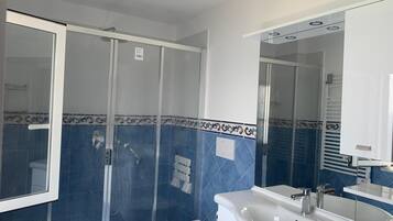 Casa de banho com chuveiro de vidro, pia branca e sanita.
