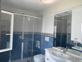 Casa de banho com chuveiro de vidro, pia branca e sanita.