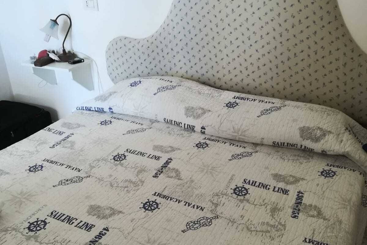 Un lit avec une couette et des oreillers à motifs nautiques, une tête de lit, une table de chevet avec une lampe et une prise électrique au mur.