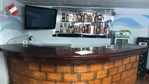 A reception area with a brick counter, a mounted TV, and shelves stocked with various liquor bottles. - Déjà Vu Backpackers (Chachapoyas)