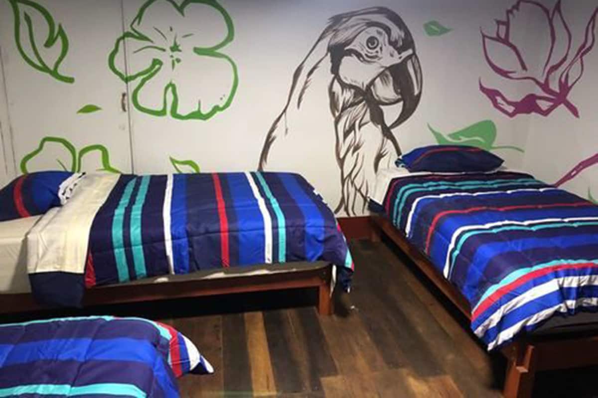 A room with two beds, each with striped bedding, a wooden floor, and walls decorated with green and pink floral patterns.