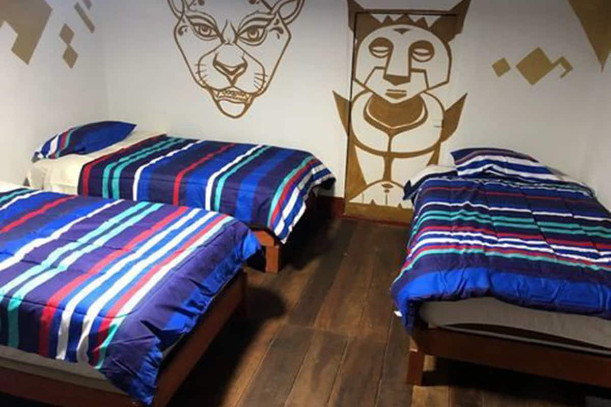 A room with two beds, each with striped bedding, wooden headboards, and a wall mural.