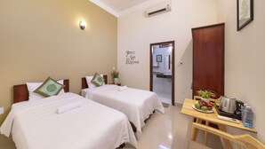 A hotel room with two beds, a small table with a kettle, a water bottle, and a plate of fruit. - Green Garden Hoi An Villa (Da Nang)