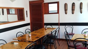 A dining area with a long wooden table, black metal chairs, and a wooden door. - Zebra Crossing Backpackers (Cape Town)