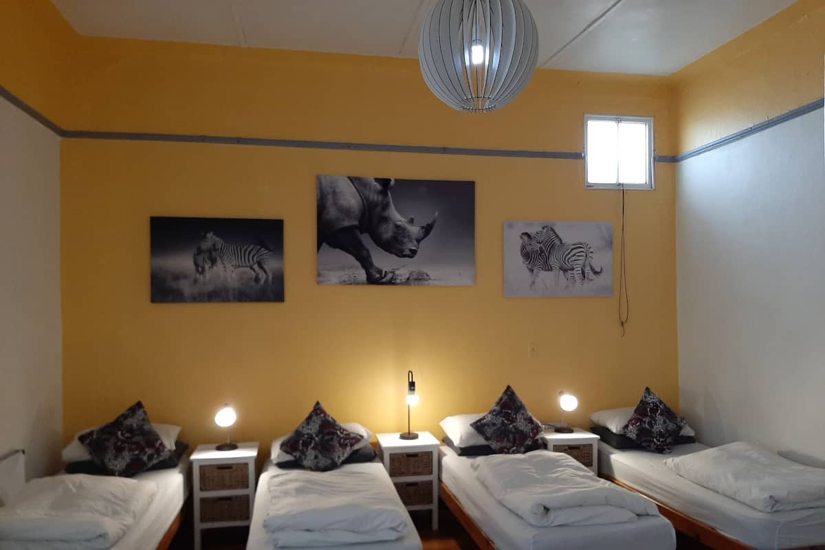 Quarto de hotel com quatro camas de solteiro, cada uma com almofada e luminária. Há três quadros de zebra fixados na parede.