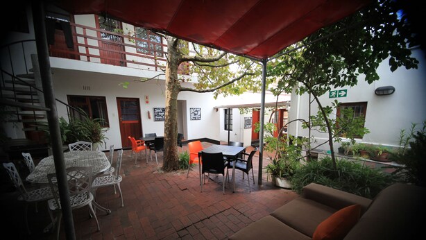 An outdoor patio area with a dining table and chairs, a sofa, and potted plants. - Zebra Crossing Backpackers (Cape Town)