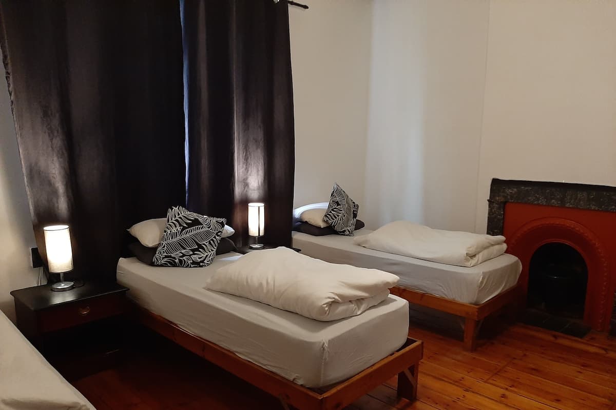 Quarto com duas camas de solteiro, mesa de cabeceira com abajur, lareira e piso de madeira.