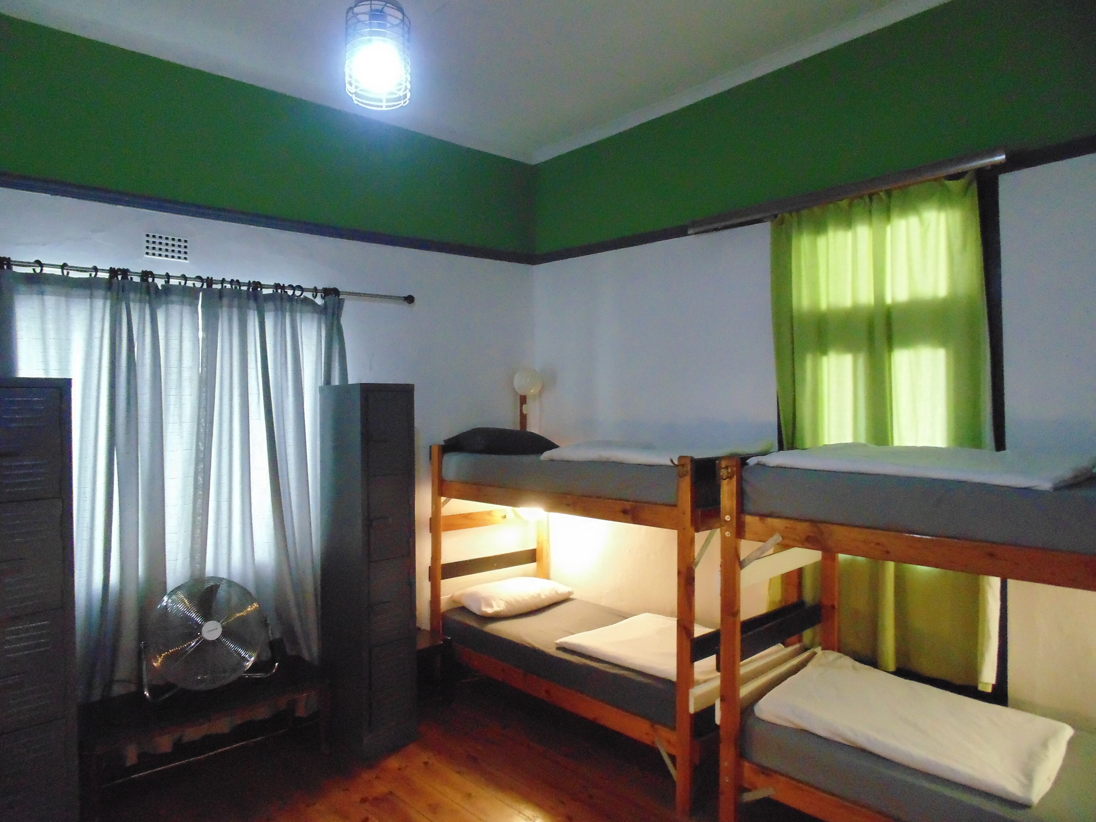 A bunk bed room with a fan, curtains, and a window with green curtains.