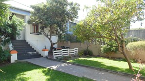 A residential property with a staircase leading to a front door, a small garden with a pathway, and a white fence. - Zebra Crossing Backpackers (Cape Town)