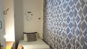 A small, single-bed room with a patterned curtain, a bedside table, and a chair.
