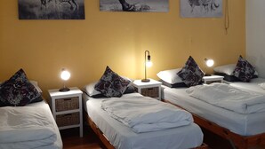A hotel room with two beds, a nightstand with a lamp, and three zebra-themed wall art pieces. - Zebra Crossing Backpackers (Cape Town)