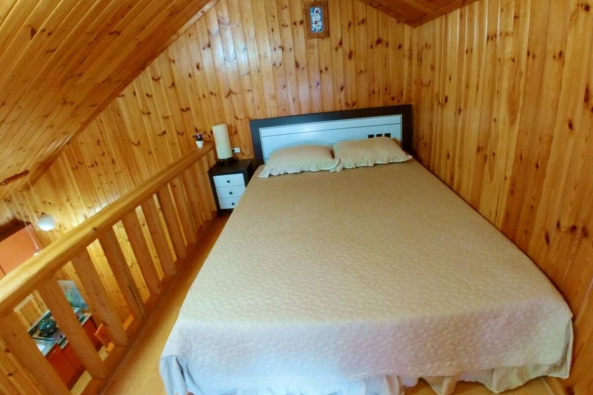 A wooden-paneled room with a bed, nightstand, and a small table with a lamp.