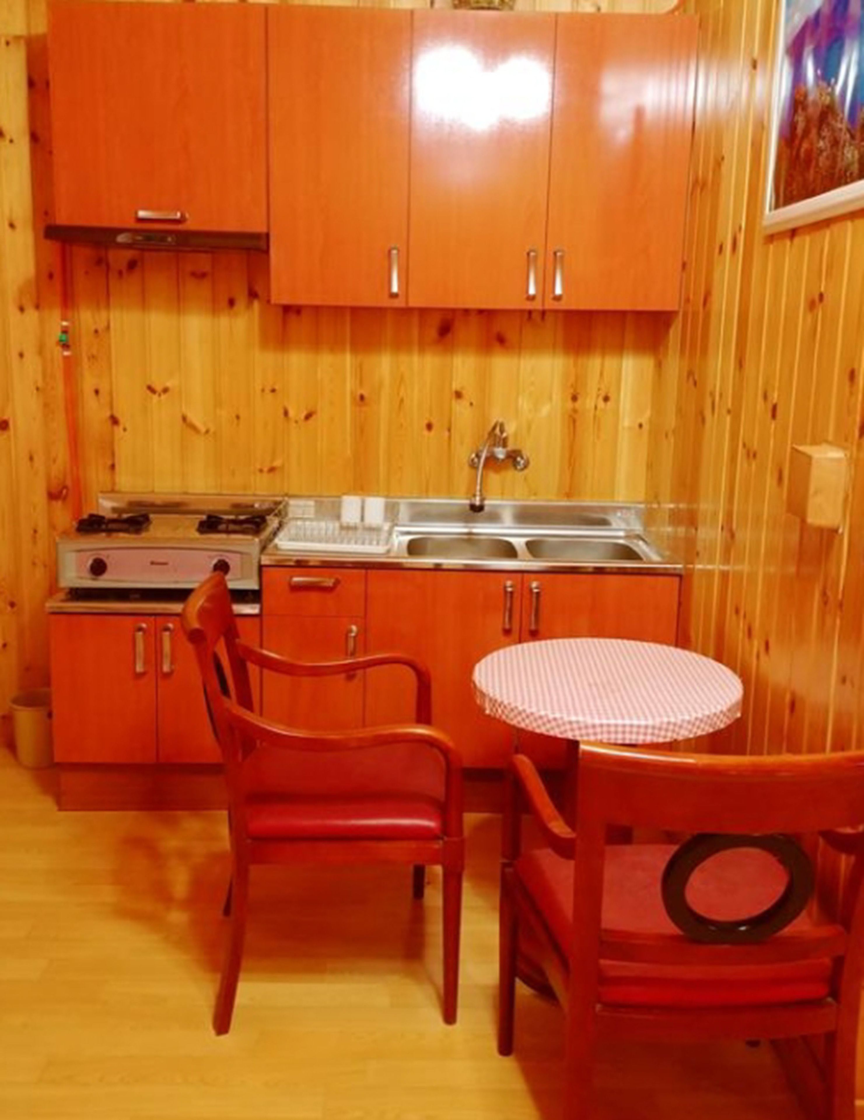 Een compacte keuken met houten kastjes, een gasfornuis, een gootsteen en een ronde tafel met stoelen.