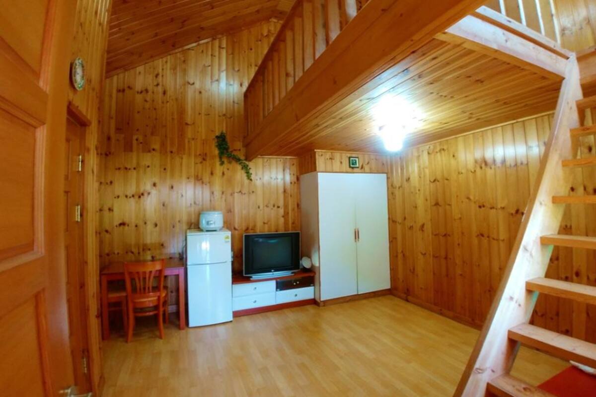 A wooden interior with a dining area, a television, a refrigerator, and a wardrobe.