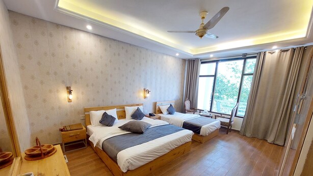 A hotel room with two beds, a wooden desk, a ceiling fan, and a large window with curtains.
